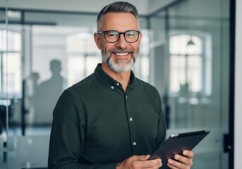 Mature businessman with glasses holding tablet smiling confidently in modern office setting showcasing professionalism and business acumen