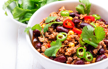 Mexican Chili con carne with beef, beans, corn, cilantro, jalapeno and tomato, white table background, top view