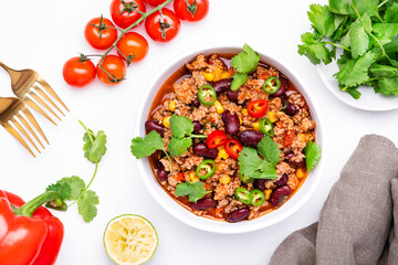 Spicy beef chili con carne with red beans, sweet corn, fresh cilantro, jalapeno pepper and tomato, served on white table, top view