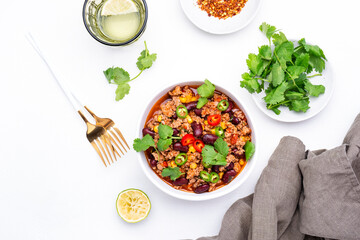 Spicy beef chili con carne with red beans, sweet corn, fresh cilantro, jalapeno pepper and tomato, served on white table, top view