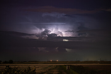 Night storm over plain land with lightning in dark sky above the horizon