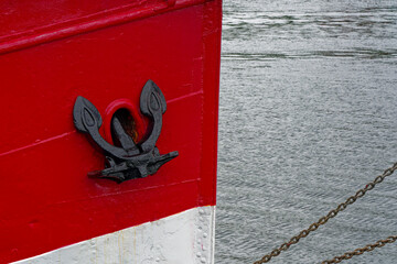 Red and white vessel in harbor with visible black anchor © Holger