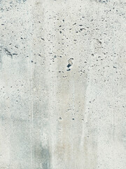 A close-up view of a pale concrete wall with small pockmarks, streaks, and weathered textures.