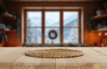 Empty wooden table with copy space for product placement in cozy alpine kitchen interior and window overlooking snowy trees and winter landscape. Seasonal advertising, home comfort, winter holidays.