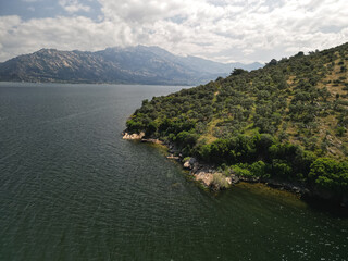 Olive covered peninsula reaches into Bafa Lake Turkey Small rocks edge the water and a shaded inlet forms a calm corner Light ripples reflect the hillside and distant peaks soften under haze