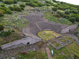 Aerial view of an ancient amphitheater in Assos Turkey with curved stone seating The area is surrounded by lush hills and scattered archaeological remains under cloudy skies