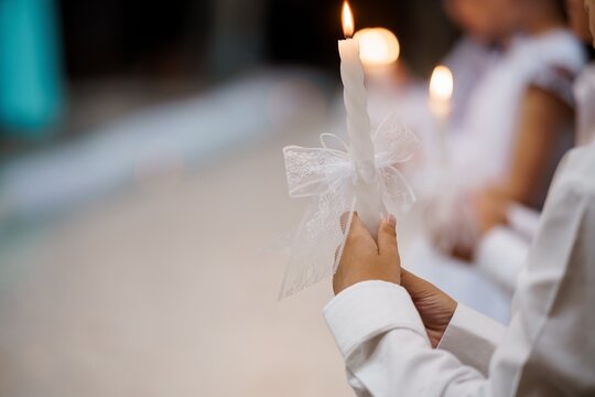 First Communion Candle Ceremony: Young Child Holding Lit White Candle with Lace Ribbon, Bright Church Interior, Religious Celebration
