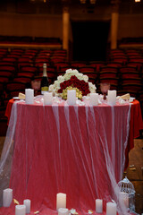 Romantic Wedding Table Setting in Theater: Red Roses, Champagne, Candles, Stage Backdrop, Elegant Celebration.