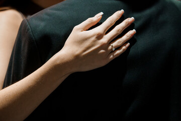 Romantic Engagement Scene: Woman's Hand with Diamond Ring on Partner's Lap, Dark Attire, Intimate Gesture, Love, Luxury.