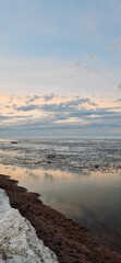 Peaceful scene of ice floes drifting in calm ocean waters with stunning sunset sky. Reflective water surface captures colorful clouds, evoking serenity and tranquility. Vertical photo