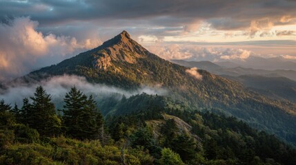 A beautiful mountain rises in the foreground surrounded by lush green forests as colorful clouds hover above during sunrise, casting a serene atmosphere over the rolling hills.