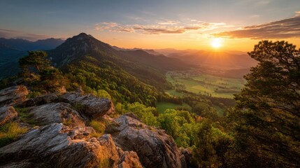 Obraz premium The sun sets behind majestic mountains, casting a warm glow over vibrant green valleys. Rocks and trees frame the picturesque view, highlighting natures beauty during twilight.