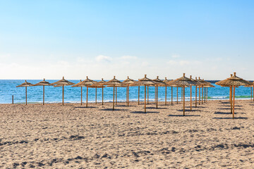 Sunny sandy beach with straw umbrellas and clear blue sea horizon