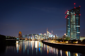 Obraz premium Frankfurt City Skyline at Night with Illuminated Skyscrapers and River Reflections