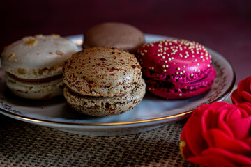 White decorative plate on burlap holds colorful macarons, creating a cozy, inviting scene. Soft textures and warm tones evoke a relaxing morning and the pleasure of sweet indulgence.