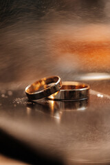 Gold wedding rings on mirror surface with warm ambient light and romantic atmosphere