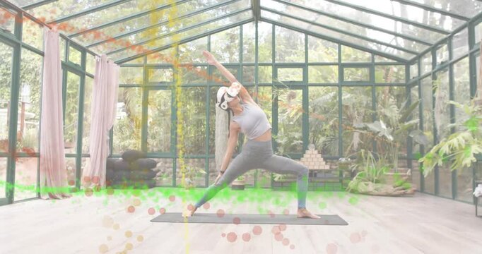 Yogi adjusting VR headset in reverse-warrior pose in greenhouse, digital particles ringing body