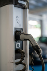 Vertical close-up of electric vehicle charging plug inserted into station indoors