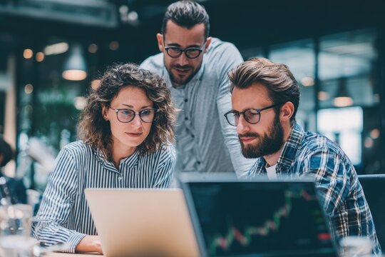 Group of professionals collaborating on a laptop in a modern office setting during a work session - Powered by Adobe