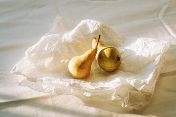 Two ripe pears on crumpled white paper in soft natural sunlight