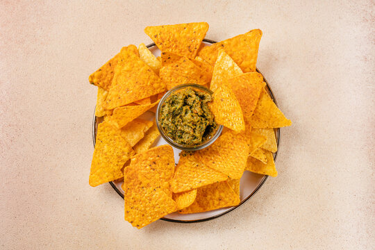 Plate of tortilla chips with green dip, flat lay