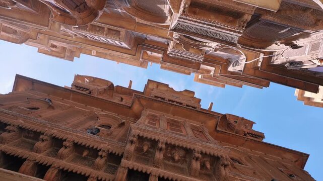 Upward view of two ornate historic Rajasthani havelis with intricate carvings, balconies, and latticework, showcasing traditional architecture and detailed stone craftsmanship.