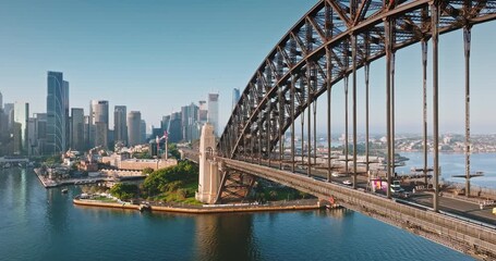 Australia, Sydney: Sydney Harbour Bridge in morning light. Cars driving traffic road connecting city skyline with surrounding urban landscape under bright blue sky. Aerial view drone flight footage - Powered by Adobe