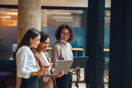 A vibrant, diverse group of professionals is actively collaborating with their laptops in a bright office environment