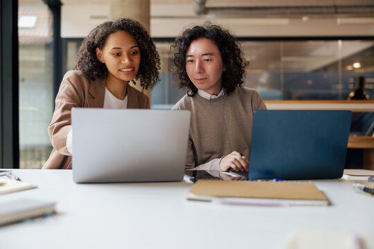 Two colleagues engaged in a productive and insightful discussion at a modern workspace with their laptops open