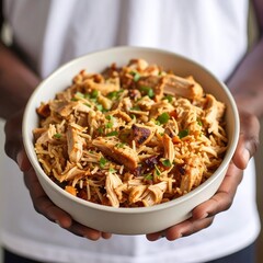 Person holding a bowl of cooked chicken and rice