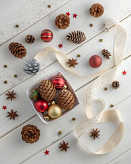 Flatlay with baubles, pinecones and ribbon on white wooden texture, cozy winter holiday mood