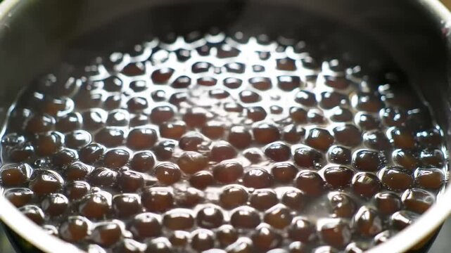 a close-up view of boba tea tapioca pearls being cooked in a pot of boiling water with a warm light reflecting off the surface creating a cozy atmosphere for a refreshing drink