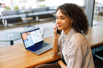 A determined woman makes an important call while efficiently working on her laptop in a stylish cafe