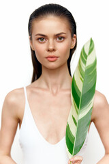 A serene woman holding a large green leaf, dressed in a minimalist white swimsuit, with a neutral...