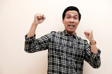 Naklejka premium Southeast Asian man wearing flannel shirt showing happy excited expression with clenched fist, on white isolated background.
