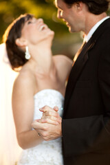 Happy Bride and Groom Slow Dancing and Laughing Together Outside - Romantic Wedding Moment - Selective Focus on Hands in Foreground
