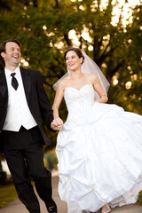 Happy Bride and Groom Holding Hands and Running Together Outside