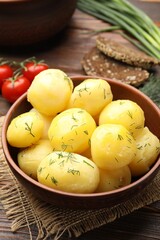 Tasty young boiled potatoes with dill and oil in bowl on wooden table, closeup