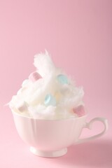 Tasty cotton candy with colorful marshmallows in cup on pink background