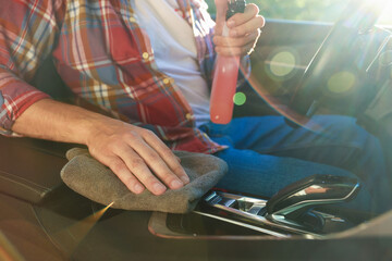 Man wiping car center console with grey microfiber rag in salon, closeup