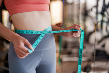 Person measuring their waist with tape measure in gym setting emphasizes importance of fitness and self care. This exercise reflects commitment to wellness and personal health goals