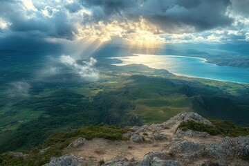 Sun rays breaking through dark clouds over a mountainous landscape with a lush green valley and a large blue lake in the distance, creating a serene and majestic atmosphere
