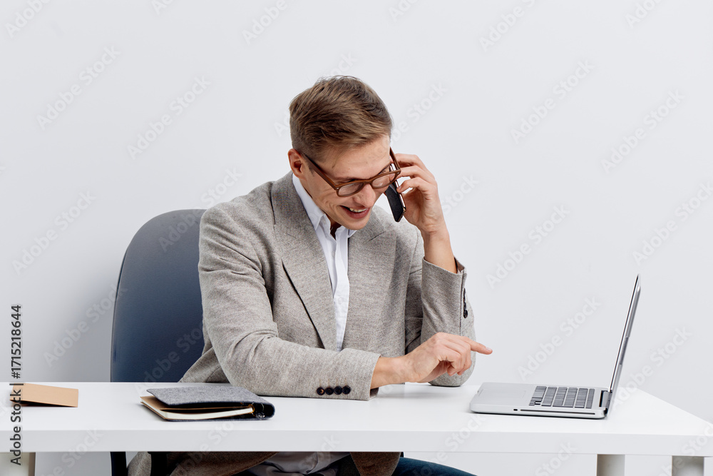 Poster professional man in glasses smiling and talking on phone while working at a desk with laptop and not