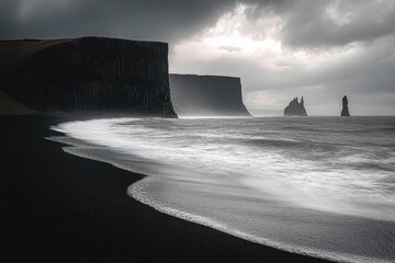 Moody black sand beach with waves washing ashore under a cloudy sky with tall dark sea cliffs and sea stacks in the distance