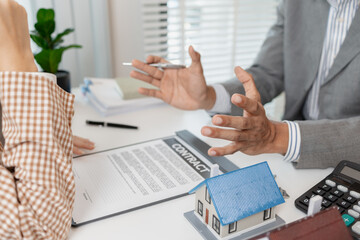 A real estate agent and client are discussing property purchase options, reviewing a contract, calculating loan terms, and considering house models as part of a housing investment decision.