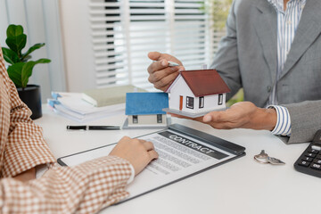 A real estate agent and client are discussing property purchase options, reviewing a contract, calculating loan terms, and considering house models as part of a housing investment decision.