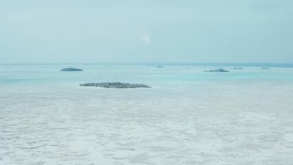 Wide shot of a serene, light-blue expanse of water with small, gray islands scattered across