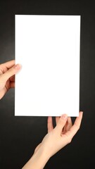 Blank white paper held by hands against dark backdrop