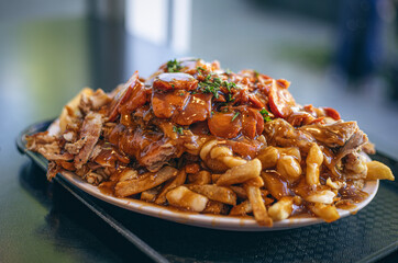 A hearty plate of loaded poutine topped with shredded meat and gravy showcases a rich mix of textures and flavors. The fries are generously covered with cheese curds and garnished with fresh herbs.