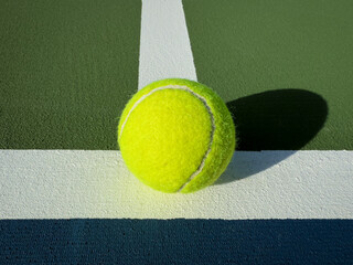 
Neon tennis ball at the junction of white court lines on textured green and blue surface, sharp afternoon shadow and minimalist sports background